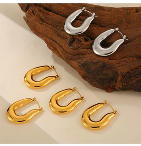 Detailed view of chunky U-shaped polished gold and silver earrings on wooden props
