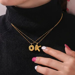 3D chunky gold bubble letter pendants O and K on a model wearing a black sweater