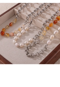 Close-up of pearl and orange agate beaded necklace with silver-tone chain on wooden box