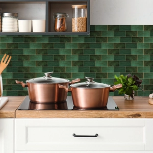 Copper kitchen cookware set with glass lids on stove against green tile backsplash