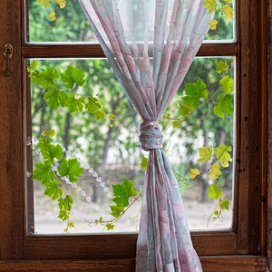 Detail of floral lace curtains with green vine decals on a rustic wooden window frame