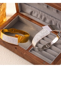 Detalle de brazalete dorado y plateado con incrustaciones de strass sobre un joyero de madera