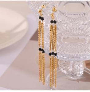 Detail of gold fringe earrings with black agate beads on a glass edge background