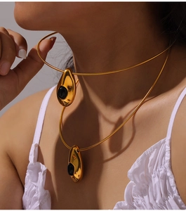 Détail de colliers serpents dorés superposés avec pendentifs gouttes en agate noire