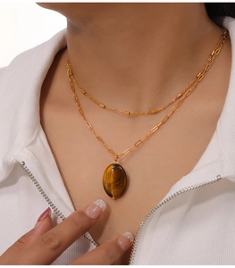 Gros plan d'un collier double épaisseur doré avec pendentif œil de tigre sur modèle