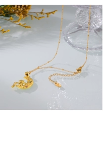 Close-up of gold moon necklace with bear and clover charms and love engraving