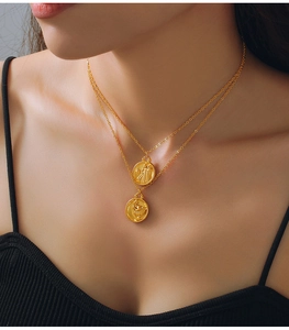 Detail of layered gold necklaces with embossed zodiac coin pendants on skin