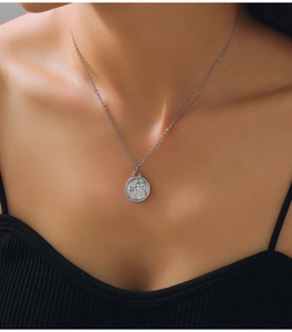 Detail of silver Gemini zodiac coin pendant on a delicate chain worn by a model