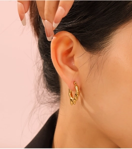 Détail d'une boucle d'oreille créole dorée irrégulière en C avec texture polie ondulée