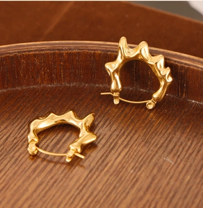 Gros plan de boucles d'oreilles créoles C dorées texturées sur plateau en bois vintage