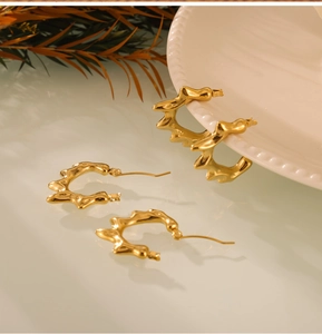 Détail macro de boucles d'oreilles créoles dorées ondulées sur support céramique