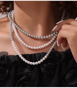 Détail d'un collier de perles multicouches gris et blanc sur mannequin en robe fleurie