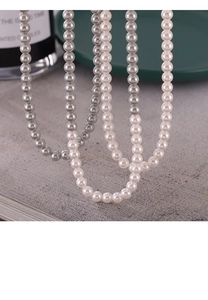 Gros plan de colliers de perles gris et crème sur une surface texturée élégante