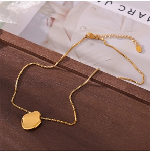 Detail van 18K vergulde geometrische hanger met box-ketting op houten dienblad