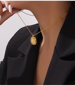 Détail du collier en acier titane plaqué or 18k avec perle sur un blazer noir chic