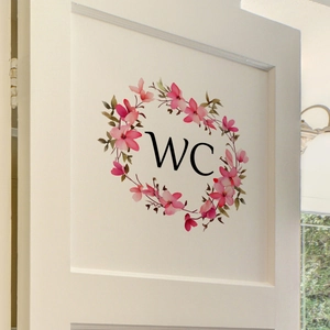 Détail d'un autocollant WC avec couronne de fleurs aquarelle rose sur une porte blanche