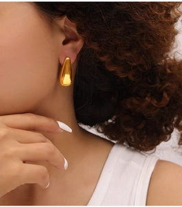 Close-up of a model wearing polished gold teardrop stud earrings in a minimalist style