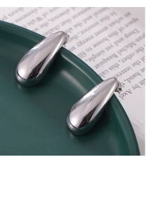 Macro detail of silver teardrop earrings with mirror finish on a ceramic plate