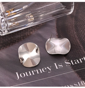 Close-up of irregular concave silver stud earrings on a dark magazine background