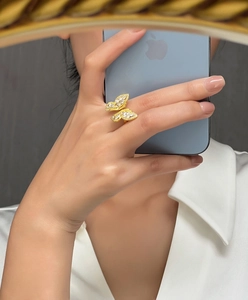 Détail d'une bague papillon dorée avec zircons blancs portée à la main devant un miroir