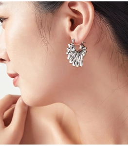 Détail de boucle d'oreille argentée polie à texture ondulée portée par un mannequin