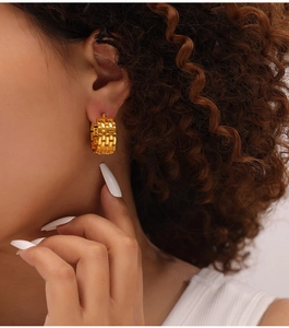 Close-up of golden C-shaped chain link hoop earrings with textured geometric pattern