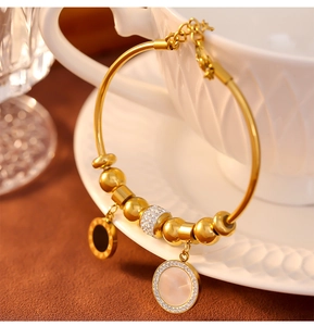 Détail du bracelet à billes dorées avec anneau à chiffres romains et pendentif blanc