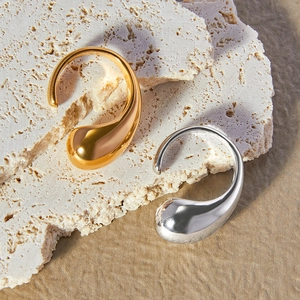 Polished teardrop ear cuffs in 18K gold and silver finishes on a textured stone surface