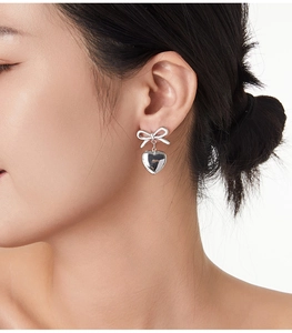Gros plan sur les boucles d'oreilles nœud et cœur en argent portées par le mannequin
