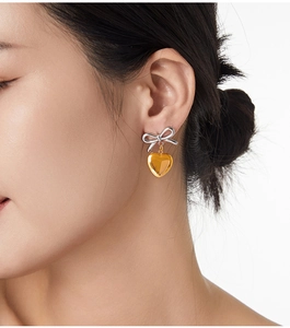 Détail de boucles d'oreilles nœud argent et cœur doré portées par un mannequin avec élégance