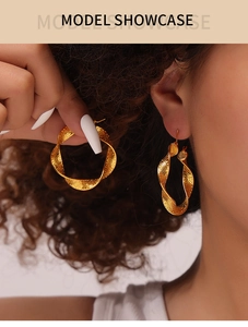 Macro shot of large golden U-shaped twisted earrings with hammered metal texture for women