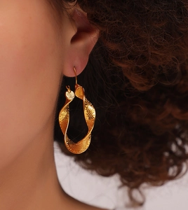 Macro detail of a gold U-shaped twisted earring with hammer texture on a female model