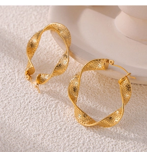 Detailed view of gold twisted hoop earrings with geometric cutout texture on light background