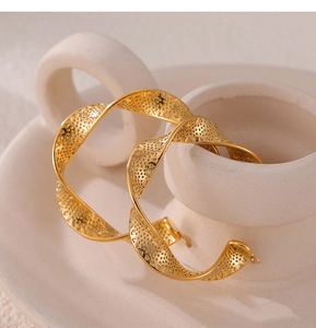 Close-up of golden U-shaped twisted hoop earrings with textured hollow patterns