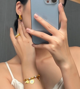 Detailed view of gold jewelry set with geometric earrings, stone ring, and charm bracelet
