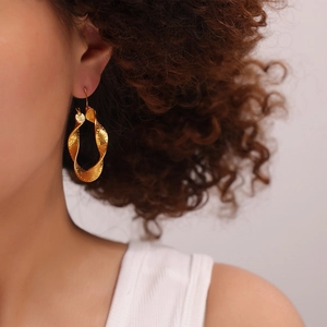 Golden twisted hoop earrings with granular texture on female model in profile view
