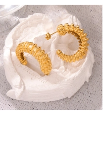 Detailed close-up of C-shaped 18k gold earrings with textured granule relief design