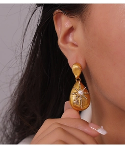 Close-up of golden teardrop earring with star engraving and pearl on model