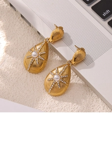 Detailed shot of golden drop earrings with shell texture, white pearl and starburst design