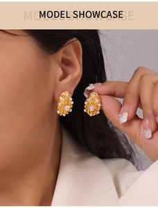 Detail of gold water-drop earrings with white pearls shown on a model's ear