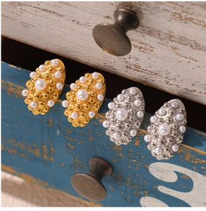 Macro shot of geometric pearl stud earrings in gold and silver finish on vintage wood