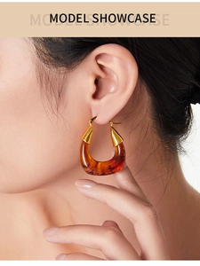 Close-up of a model wearing U-shaped amber resin earrings with golden metal accents