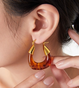 Detail view of large U-shaped earrings featuring amber resin and polished gold plating
