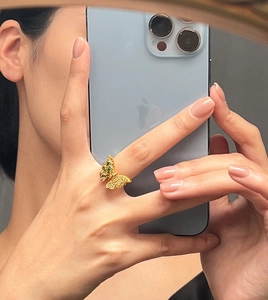 Primer plano de anillo mariposa dorado con cristales verdes y circonitas