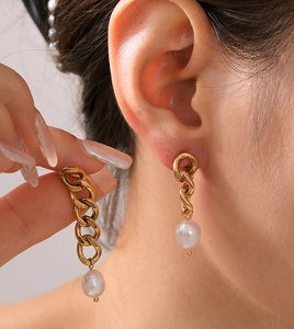 Detailed view of gold chain earrings featuring white baroque freshwater pearls on a model
