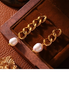 Macro shot of gold plated chain earrings with freshwater pearls on wooden jewelry box