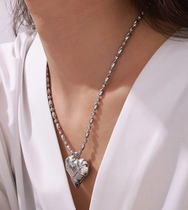 Close-up of hollow heart pendant with geometric texture on beaded chain necklace