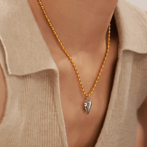 Collier en perles d'acier doré 18 carats avec pendentif cœur argenté porté par un mannequin