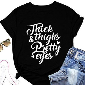 Flat lay of black T-shirt with 'Thick thighs & Pretty eyes' text and chic accessories