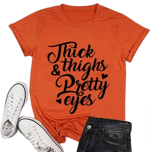Flat lay of orange cotton T-shirt with Thick Thighs Pretty Eyes print and black denim shorts